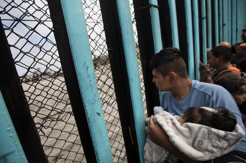 ** HOLD FOR OVERNIGHT STORY ** File - In this April 29, 2018 file photo, a member of the Central American migrant caravan, holding a child, looks through the border wall toward a group of people gathered on the U.S. side, as he stands on the beach where the border wall ends in the ocean, in Tijuana, Mexico, Sunday, April 29, 2018. The group that led a monthlong caravan of Central Americans seeking asylum in the United States wanted to draw attention to the plight of people in the violent region. (AP Photo/Hans-Maximo Musielik, File)