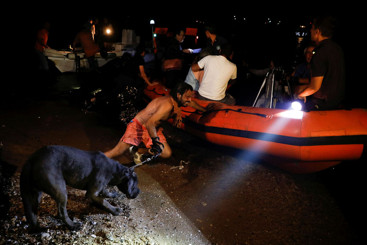 A man holding a dog pushes an inflatable boat as locals are evacuated during a wildfire at the village of Mati, near Athens, Greece, July 23, 2018. REUTERS/Alkis Konstantinidis - RC1585A91650